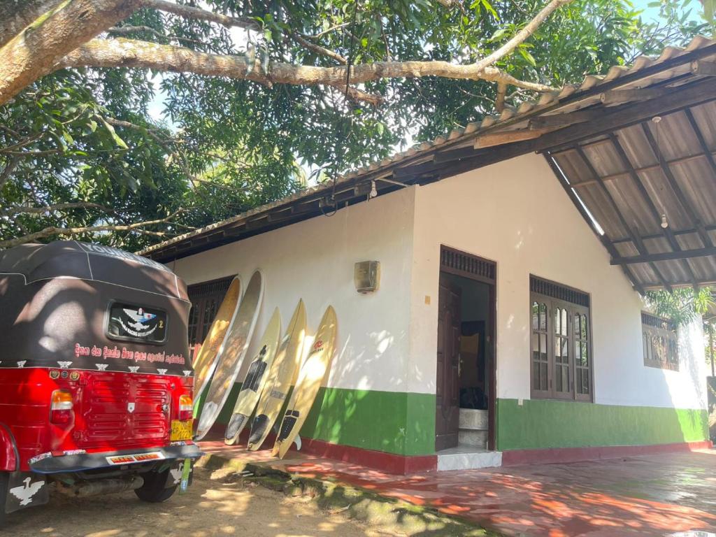 Una furgoneta roja aparcada frente a un edificio con tablas de surf. en Kuma Surf Camp Hostel, en Weligama