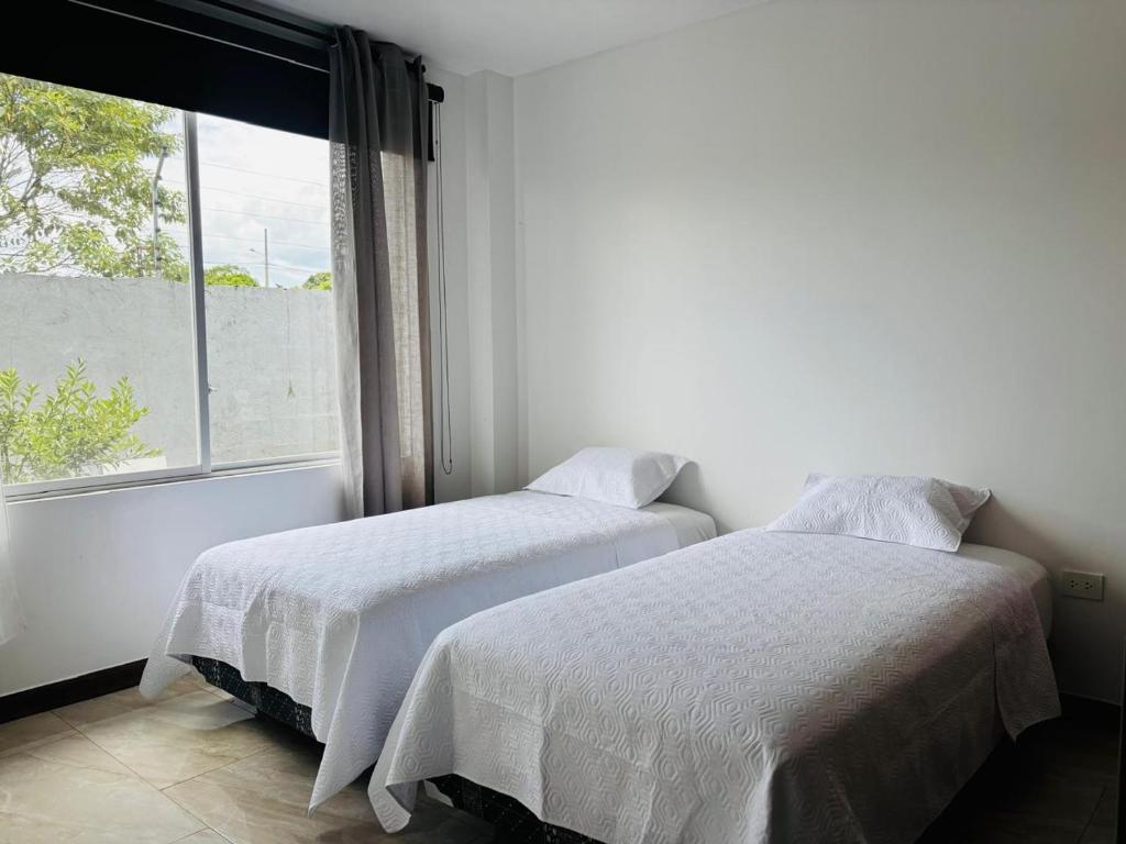 two beds in a white room with a window at Casa en Puyo Amazonía "Villa Coral" in Puyo