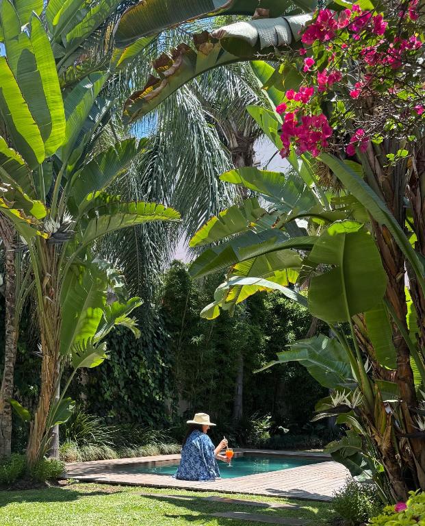 a woman in a hat sitting next to a swimming pool at Villa Vicuña Salta Hotel Boutique in Salta