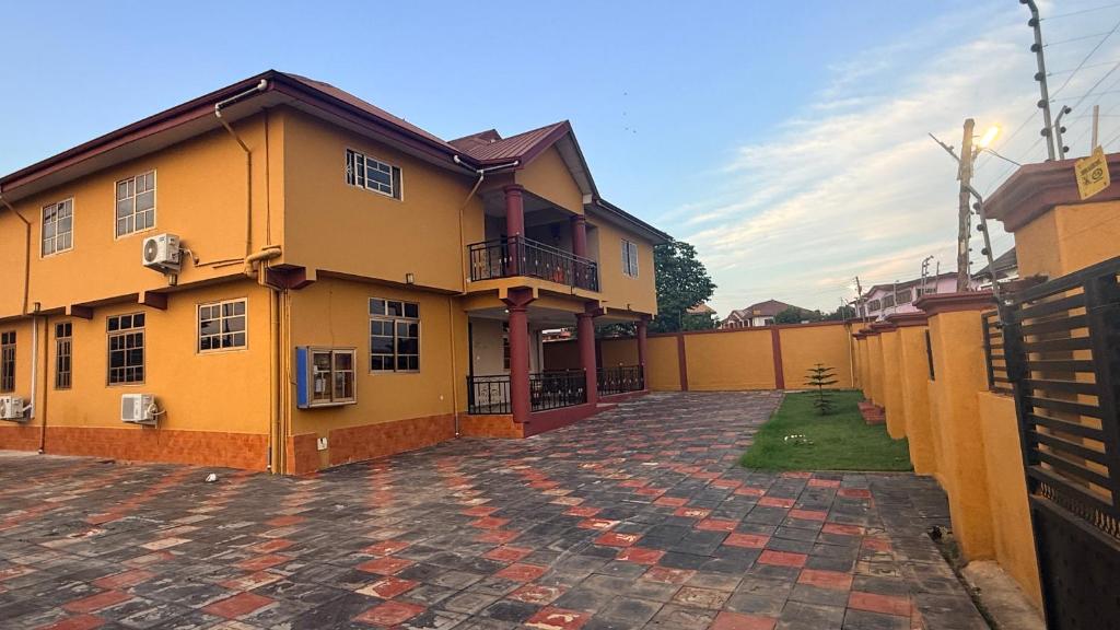 a large yellow building with a brick courtyard at LOUNEL BnB in Kumasi