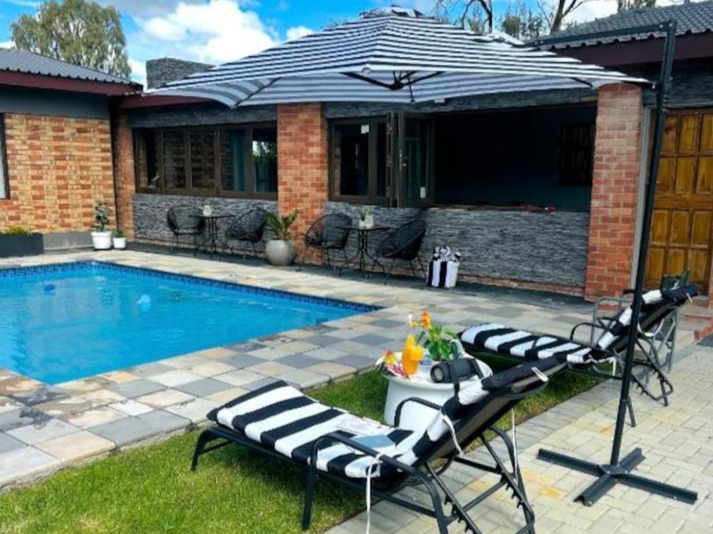 a swimming pool with two lounge chairs and an umbrella at Hope Villa Luxury Accomodation in Odendaalsrus
