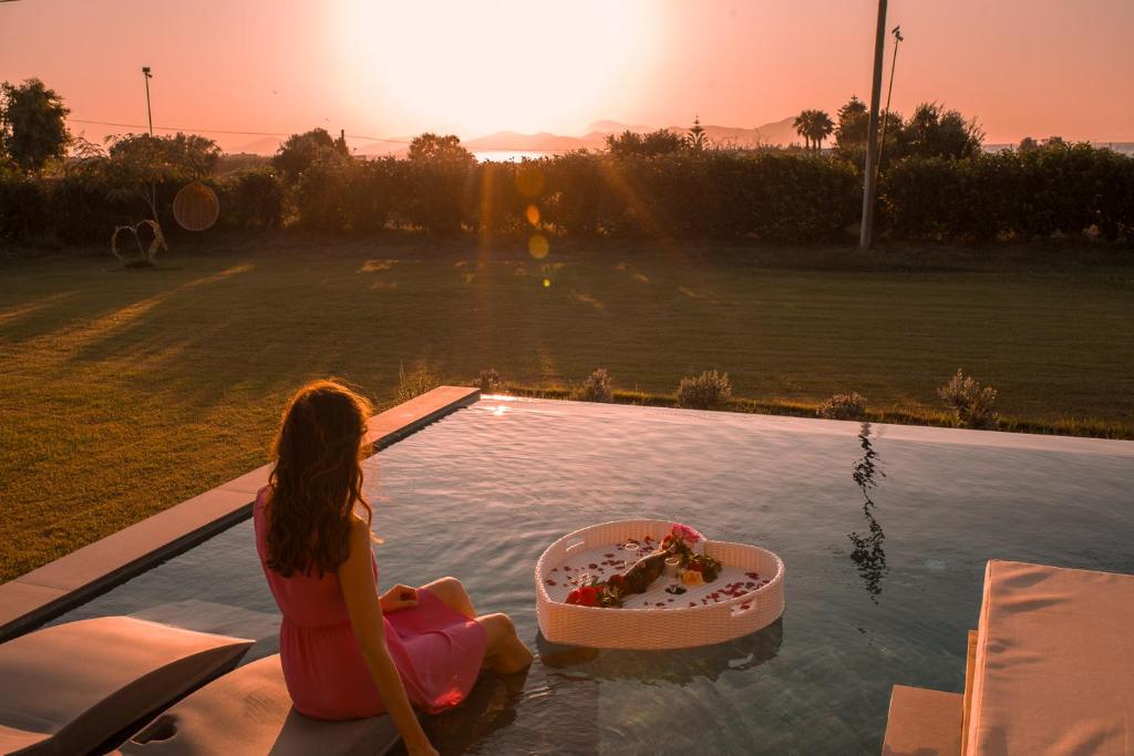 a woman sitting on the edge of a swimming pool with a cake in a bowl at Aphrodite Luxury Suites with private heated pools in Kos Town