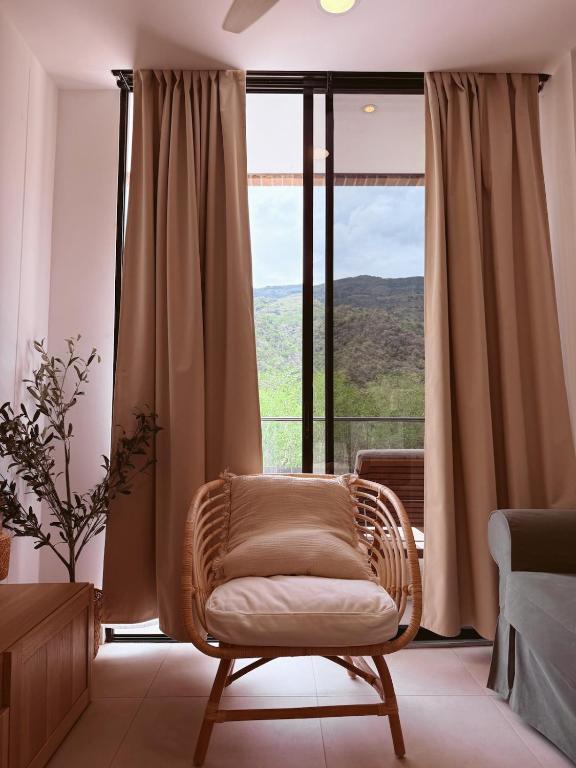 a wicker chair sitting in front of a large window at KOA Villeta - Loft y terraza con vista a la montaña in Nimaima