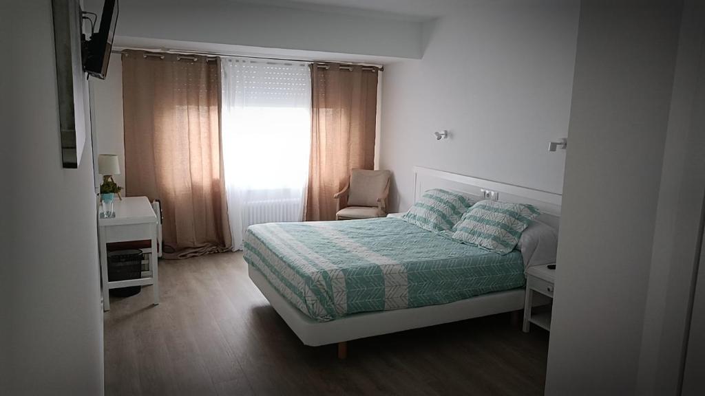 Un dormitorio con una cama, una silla y una ventana en La mesa del cocinero, en Lugo