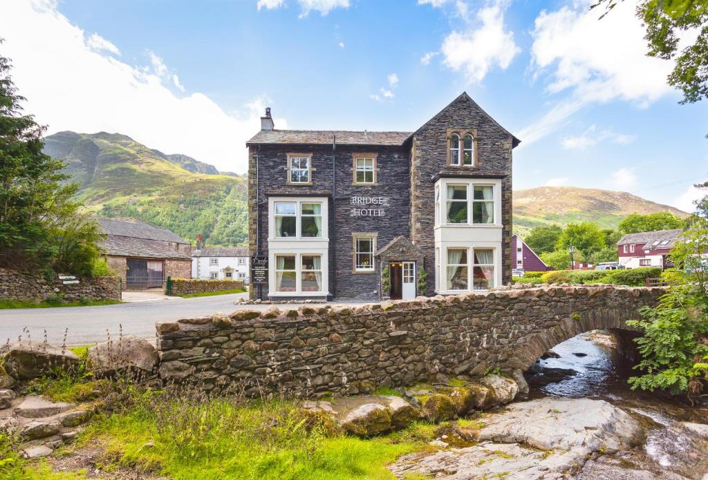 un puente de piedra frente a una casa con una pared de piedra en Bridge Hotel, en Buttermere