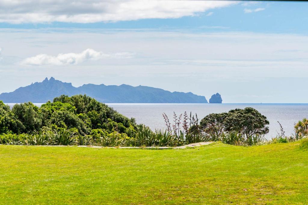 ein grasbewachsener Hügel mit Blick auf das Meer und die Berge in der Unterkunft Private Beach Access - Mangawhai in Mangawhai