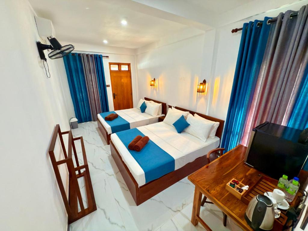 a bedroom with a bed and a table and a television at Devon Surf . Inn - Hiriketiya in Dickwella
