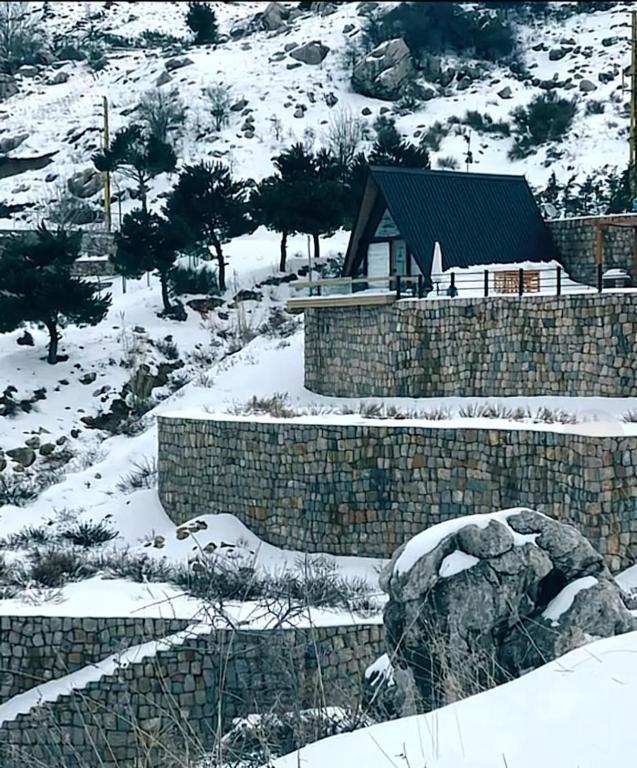 a snow covered yard with a stone wall and a house at Là Guesthouses in ‘Aynţūrah