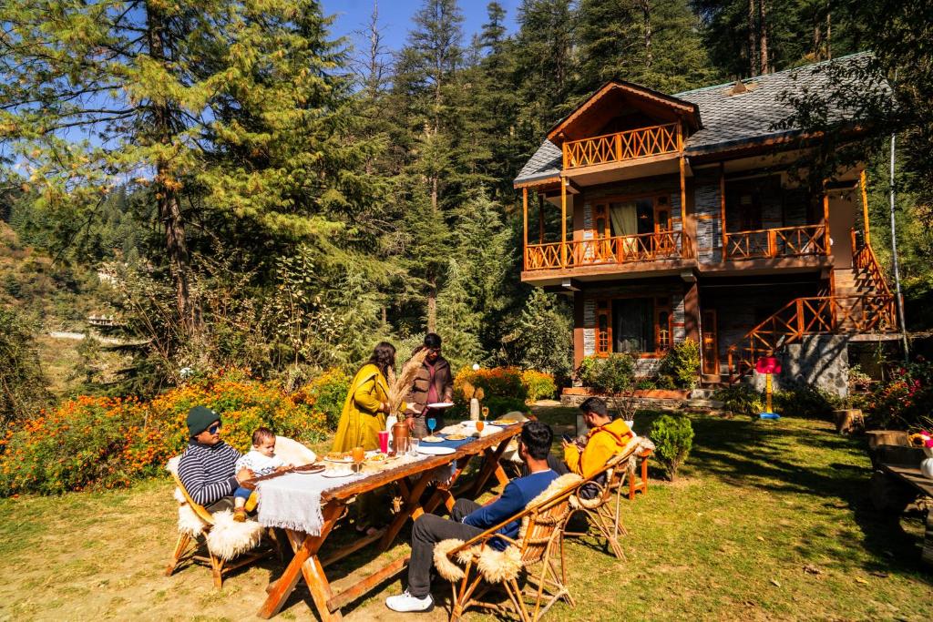 a group of people sitting around a table in front of a house at Doghari Chalets Jibhi by Himtrek Stays in Jibhi