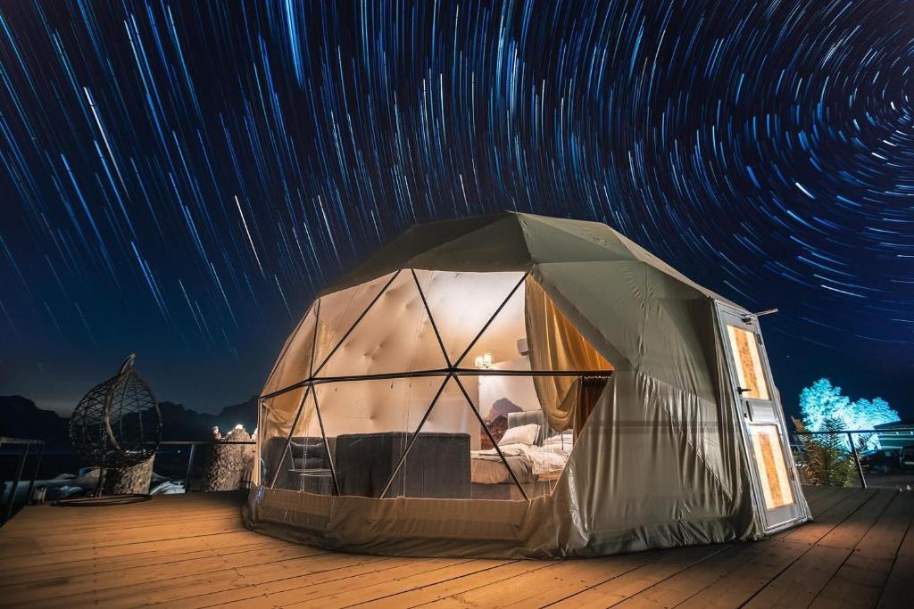 Una tienda de campaña colocada en una terraza bajo los rastros de estrellas. en DESERT ROSE lUXURY CAMP, en Wadi Rum