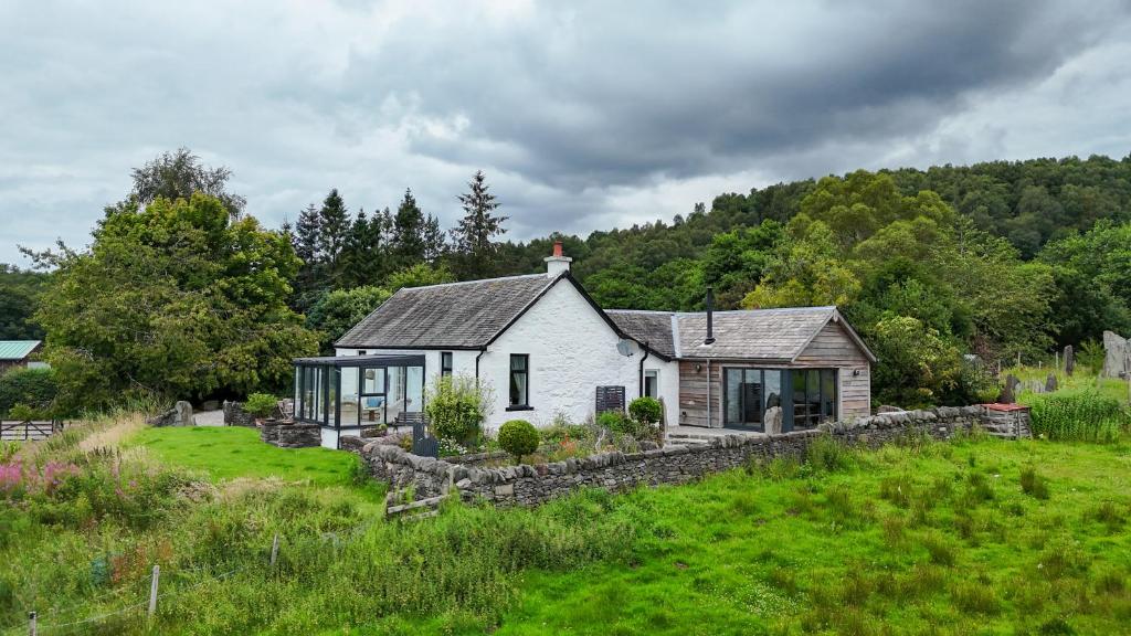 une maison blanche avec un mur en pierre dans un champ dans l'établissement Blair Cottage, à Rowardennan