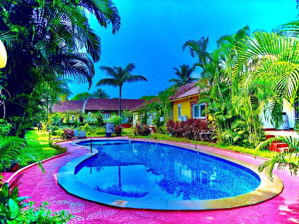 a swimming pool in front of a house with palm trees at Sana Villa & Resort Goa in Anjuna