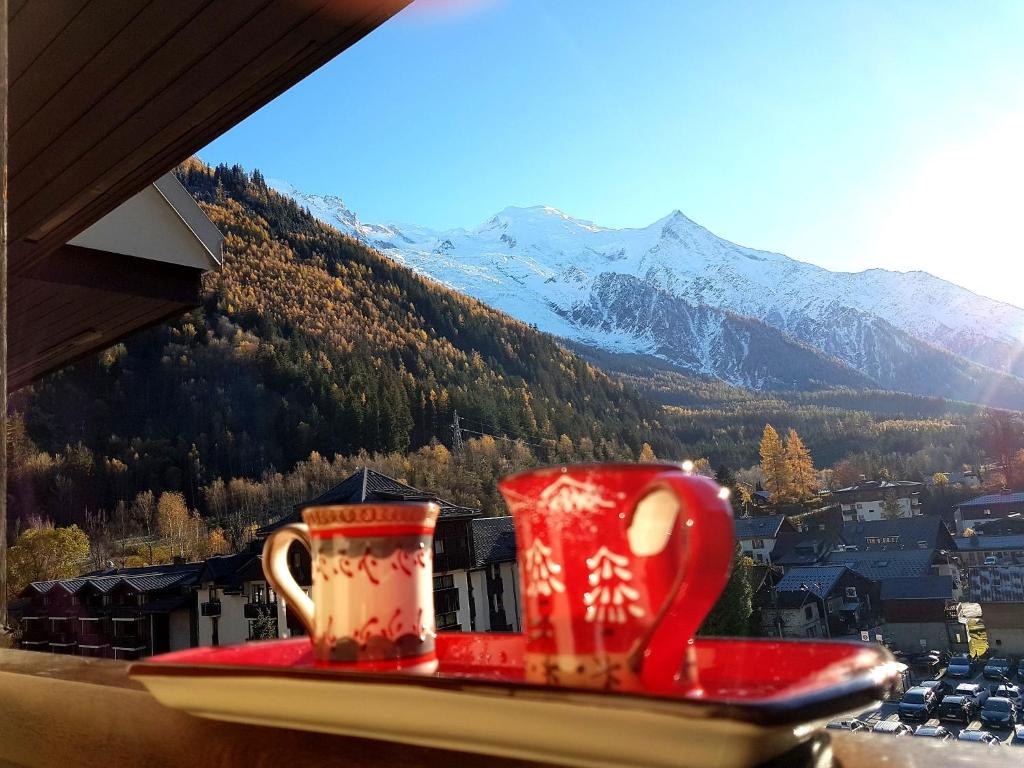 two coffee mugs sitting on a window sill with a mountain at Le Chamois 5E Balcon panoramique MontBlanc avec parking gratuit in Chamonix-Mont-Blanc