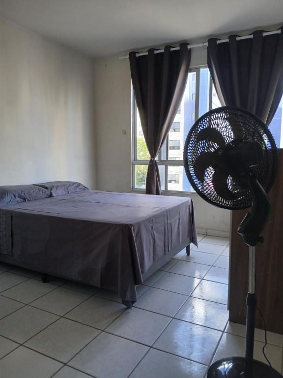a bedroom with a bed and a fan in front of a window at Quarto aconchegante na melhor localização do Recife in Recife