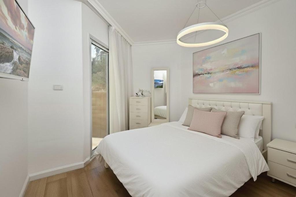 a white bedroom with a white bed with a pink pillow at sea of Galilee 612 in Tiberias