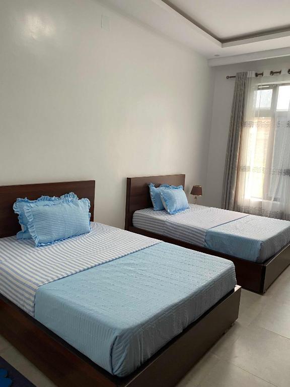 two beds in a bedroom with blue pillows at maman home apartment in Gisenyi