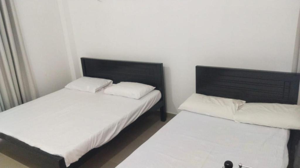 two beds in a small room with white sheets at Moon Guest House in Trincomalee