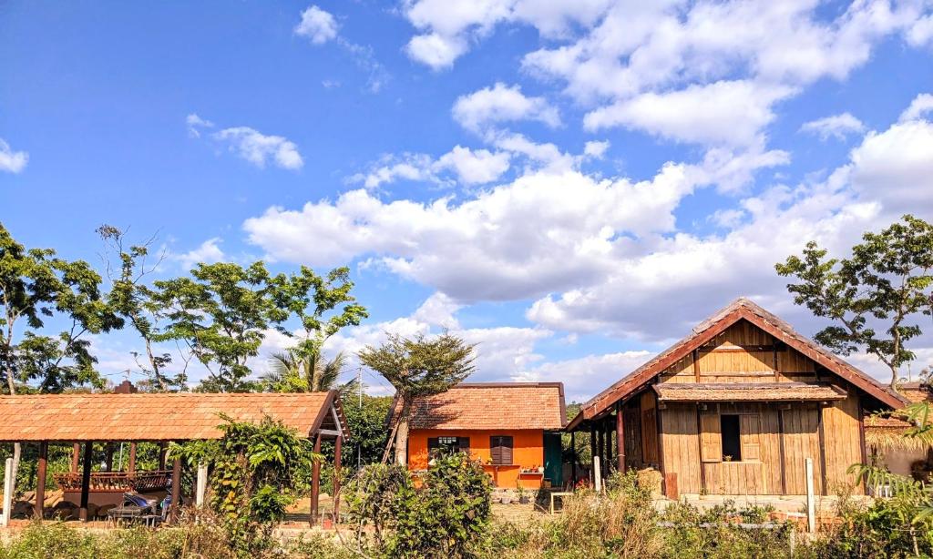 a couple of houses in a field with a cloudy sky at Charming Wooden House with Herbal Farm Vibes in Bao Loc