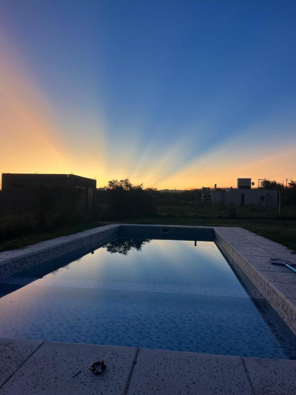 a swimming pool with a sunset in the background at Mía Casa de Campo in Unquillo