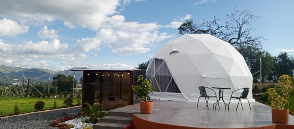 een witte koepeltent met twee stoelen op een terras bij La cabaña de Ciela Glamping con jacuzzi in Latacunga
