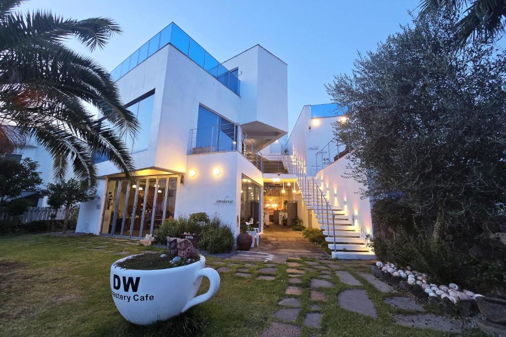 Ein weißes Haus mit einer Kaffeetasse im Garten in der Unterkunft Seogwipo Dawa Pool Villa Pension in Seogwipo