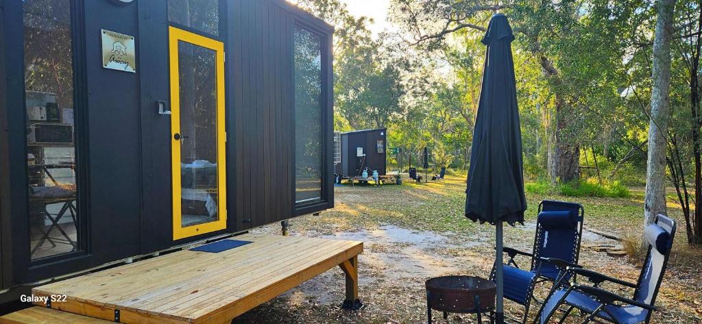 a black tiny house with a bench and an umbrella at Wilderness Whisper By Tiny Away in Agnes Water