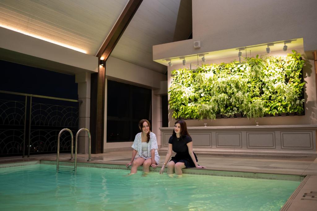two women sitting on the edge of a swimming pool at Paxtonz Suites,1Utama,IKEA Damansara,SEGi,Desa Park in Petaling Jaya