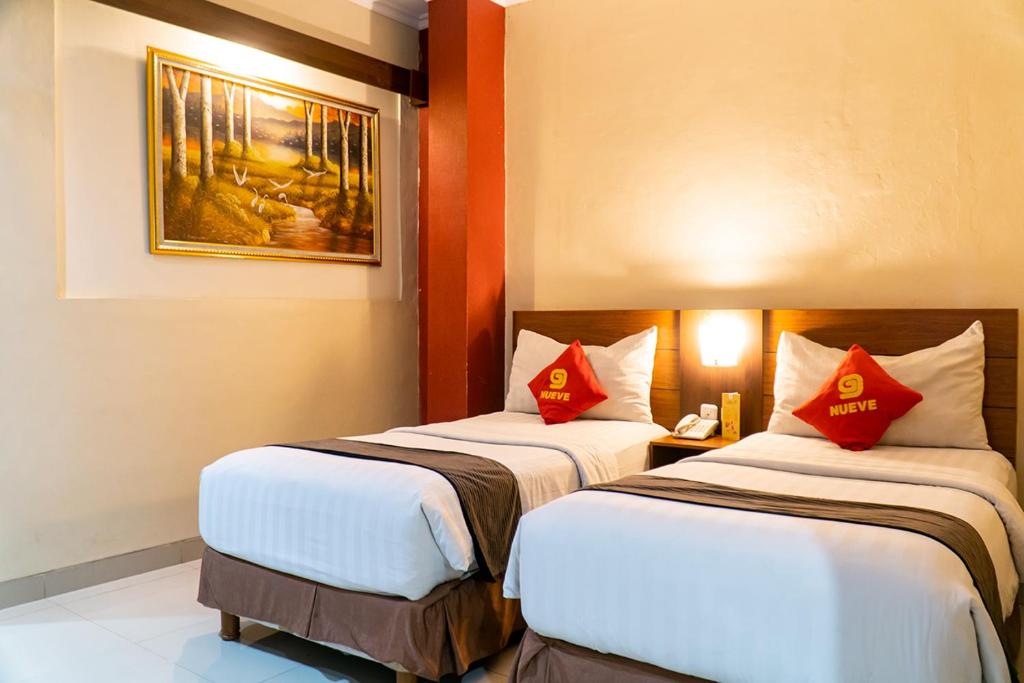 two beds in a hotel room with red pillows at Nueve Malioboro Hotel Yogyakarta in Yogyakarta