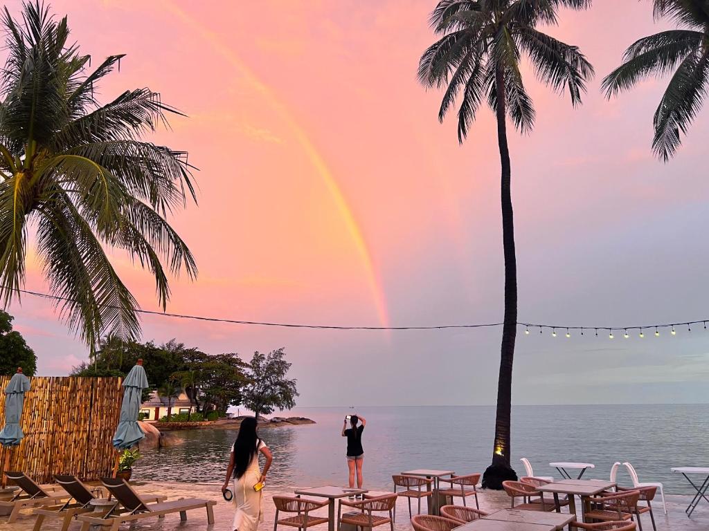 a rainbow over a beach with tables and palm trees at Three Trees Samui Resort - Sarocha Villa in Lamai