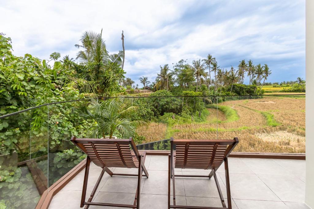 two chairs sitting on a balcony looking out at a field at Bale Marva, Gianyar - Modern Tropical Hideaway near Ubud & Bali Safari Park in Lebih