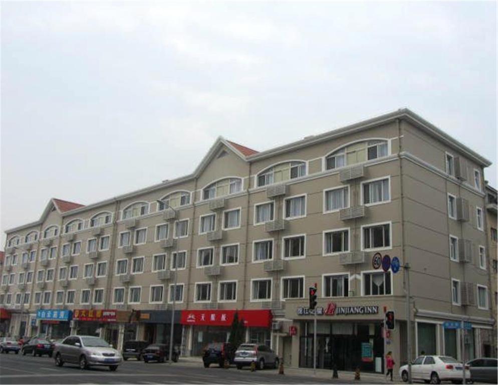 duży budynek przy ulicy miejskiej z zaparkowanymi samochodami w obiekcie Jinjiang Inn Dalian Lianhe Road w mieście Dalian