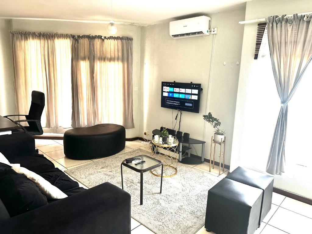 un soggiorno con un divano nero e una TV di Feel At Home Cosy Apartment a Gaborone