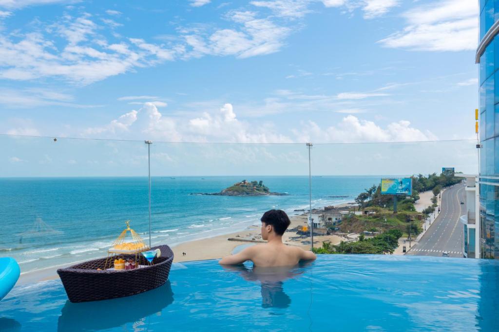 un homme dans une piscine avec vue sur l'océan dans l'établissement ONE SEASON BOUTIQUE HOTEL Vung Tau - BEACHFRONT, à Vung Tau