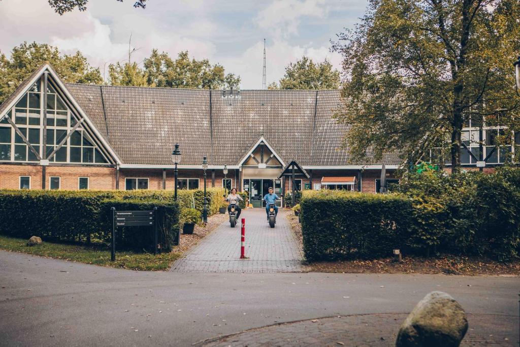 two people riding motorcycles in front of a building at Stuifzand Bungalow | 8 personen in Hooghalen