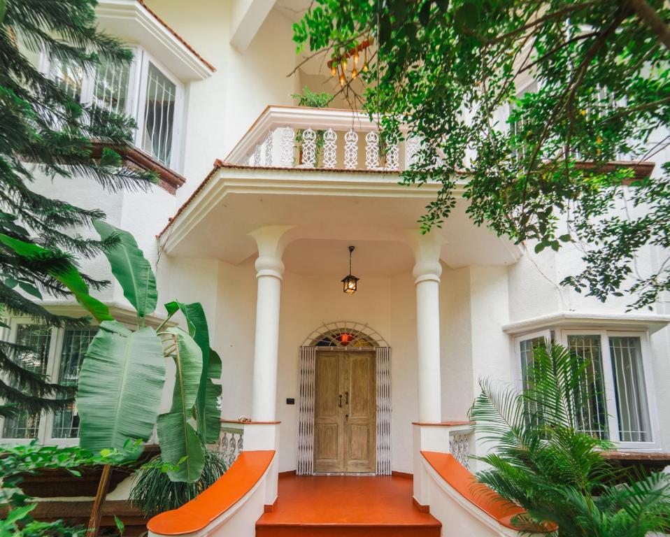 a white house with a wooden door and trees at Villa Sylvana By Bluewave Hospitality in Nagoa-Bardez