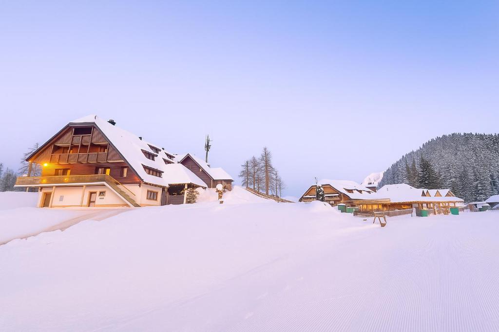 a snow covered hill with a house in the background at Hotel Krvavec in Cerklje na Gorenjskem
