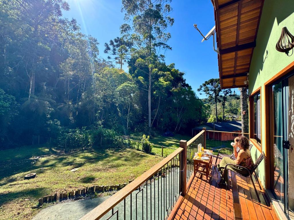 a woman sitting at a table on a deck with a view at Visconde da Mata Chalés Maringá MG in Visconde De Maua