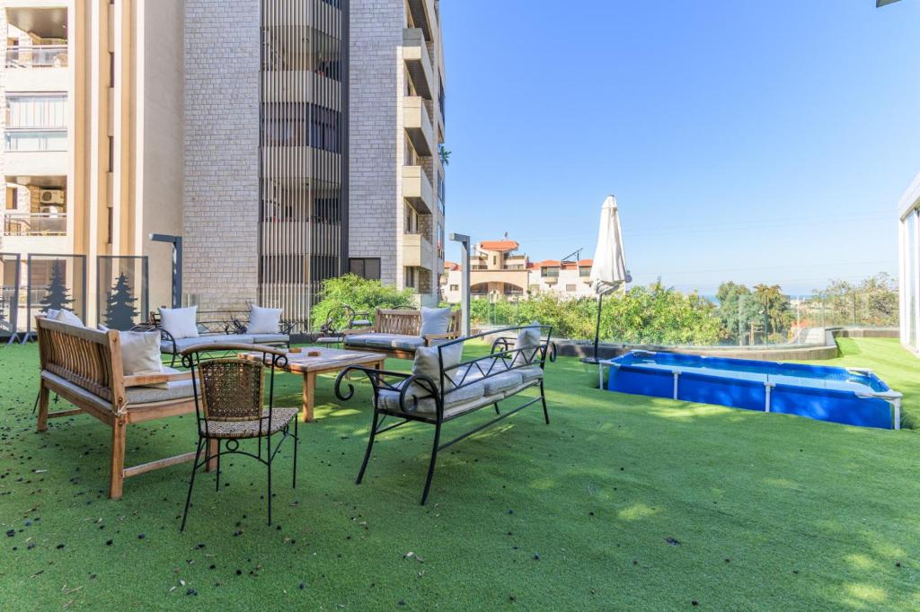 a patio with a table and chairs on the grass at GlassHaus Rooftop 2-BR W Pool & Terrace in Ghazir in Admā
