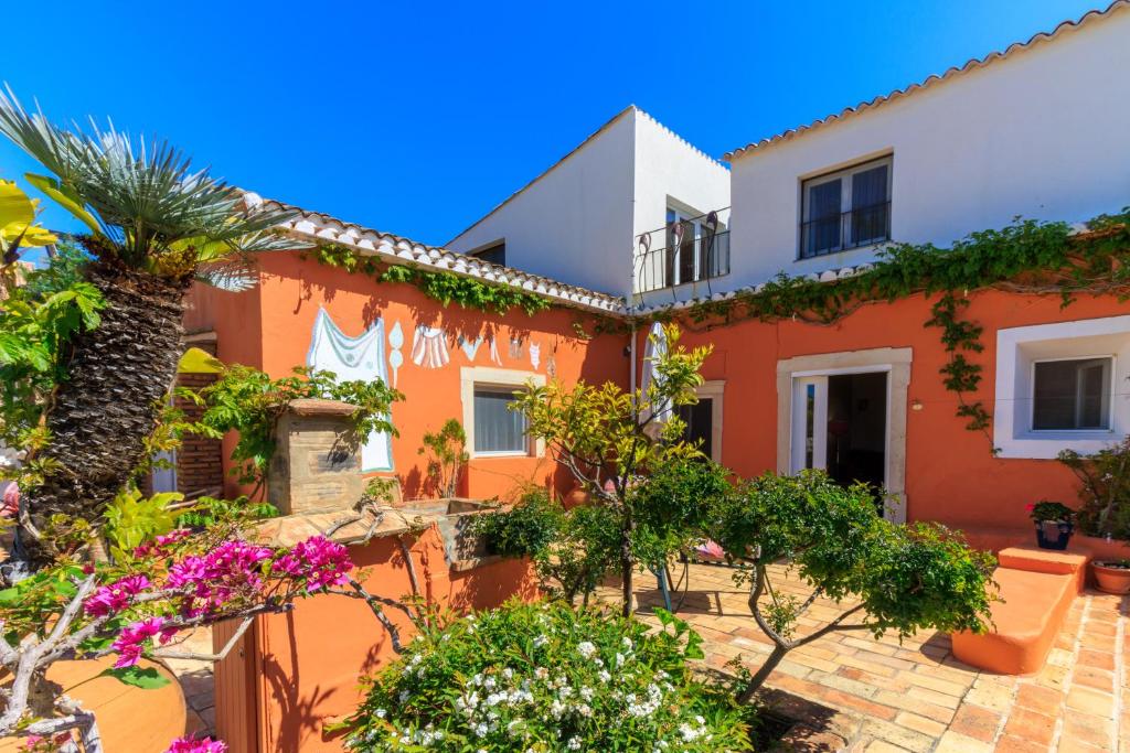 een oranje en wit huis met bomen en bloemen bij Quinta dos Amigos in Almancil