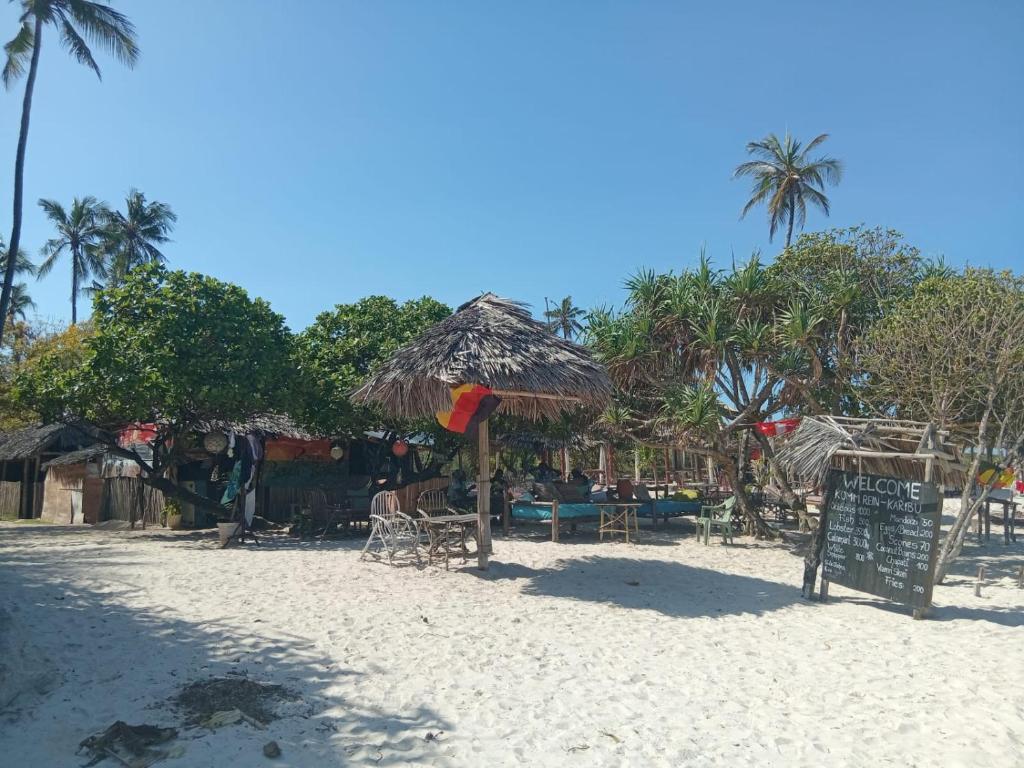 a beach with a straw umbrella and chairs and a sign at Tango house in Ukunda