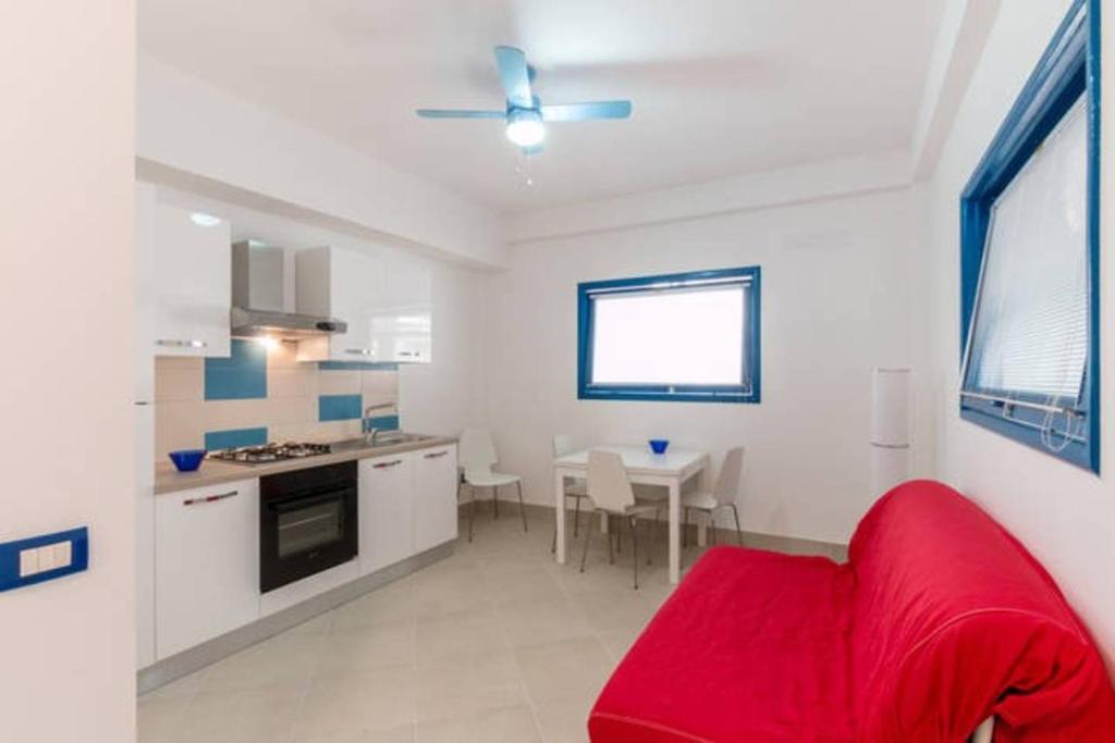 een woonkamer met een rode bank en een keuken bij Bilocale Scoglitti nei luoghi di Montalbano in Scoglitti