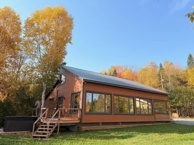 a small house with a large deck and windows at Le Domaine Riverin in Pohénégamook