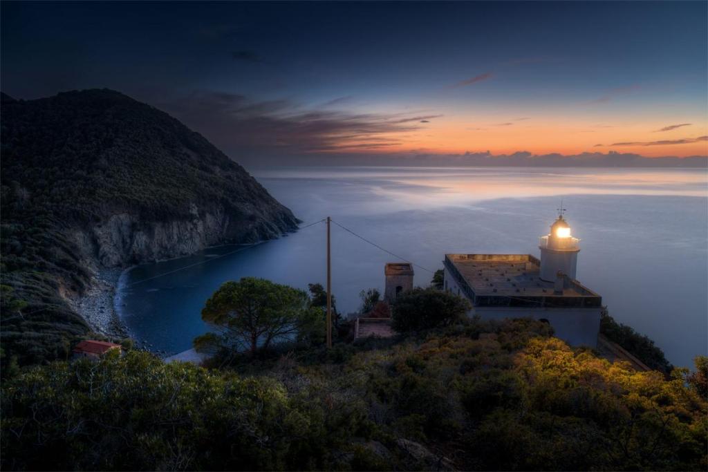 a lighthouse on a hill with a body of water at Patresi Mare - Goelba in Mortigliano