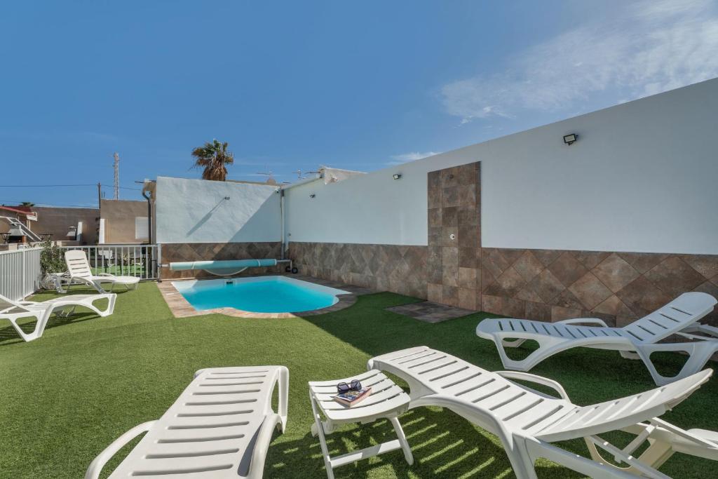Un patio con sillas blancas y una piscina. en 2 Apartamentos Omanai Tenerife Sur, en Las Galletas