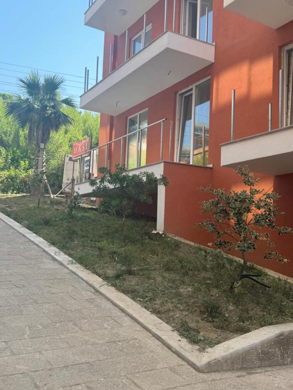 a red building with a palm tree next to a sidewalk at Sea view in Shëngjin