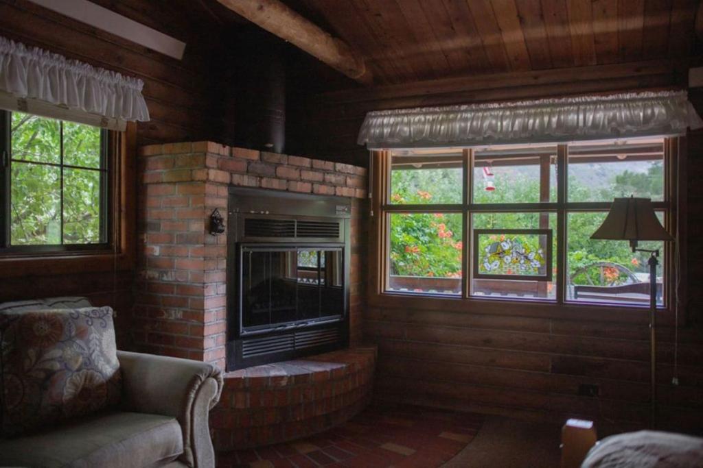 a living room with a brick fireplace and windows at HONEYSUCKLE - Rustic cabin for 2 in Oak Creek Canyon in Indian Gardens