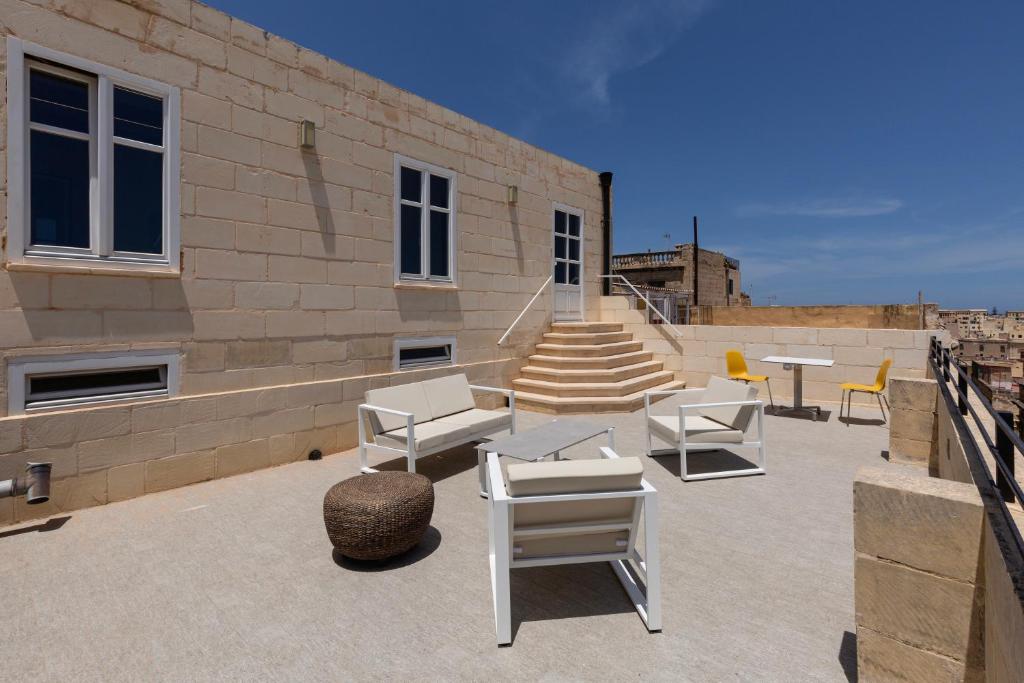 Un patio con sillas y mesas blancas y escaleras. en The Glen Residences, en Senglea