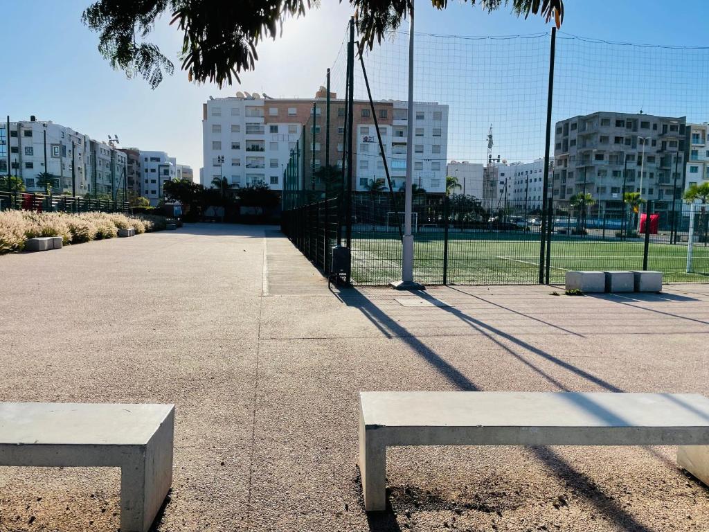 Deux bancs dans un parc avec des bâtiments en arrière-plan dans l'établissement Cozy apartment, in secure residence, à Agadir