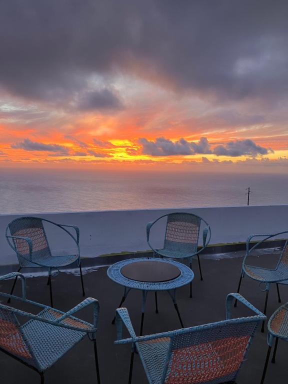 eine Gruppe von Stühlen und Tischen auf einem Balkon mit Sonnenuntergang in der Unterkunft Ocean Retreat in Fajã da Ovelha