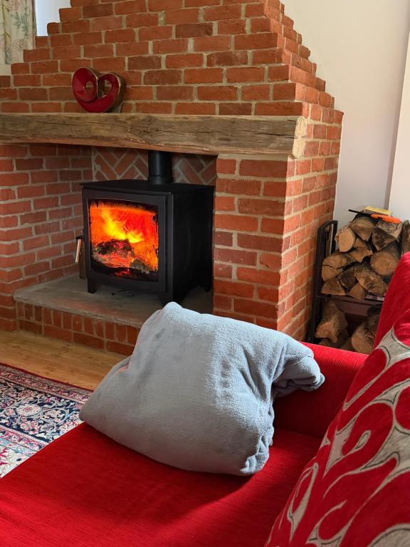 a brick fireplace with a pillow on a red couch at 2 Bed Rural Retreat Alpacas, Privare hot tub Dorset christmas break and a cosy wood burner in Horton
